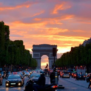 Vivid sunset sky over Arc de Triomphe, capturing Parisian traffic and architecture.