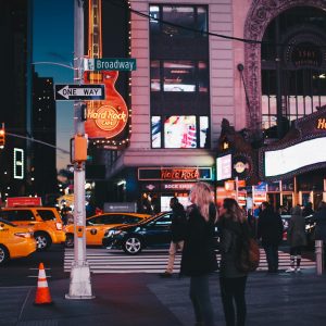 A bustling street view of Broadway at night featuring Hard Rock Cafe, taxis, and pedestrians in New York City.